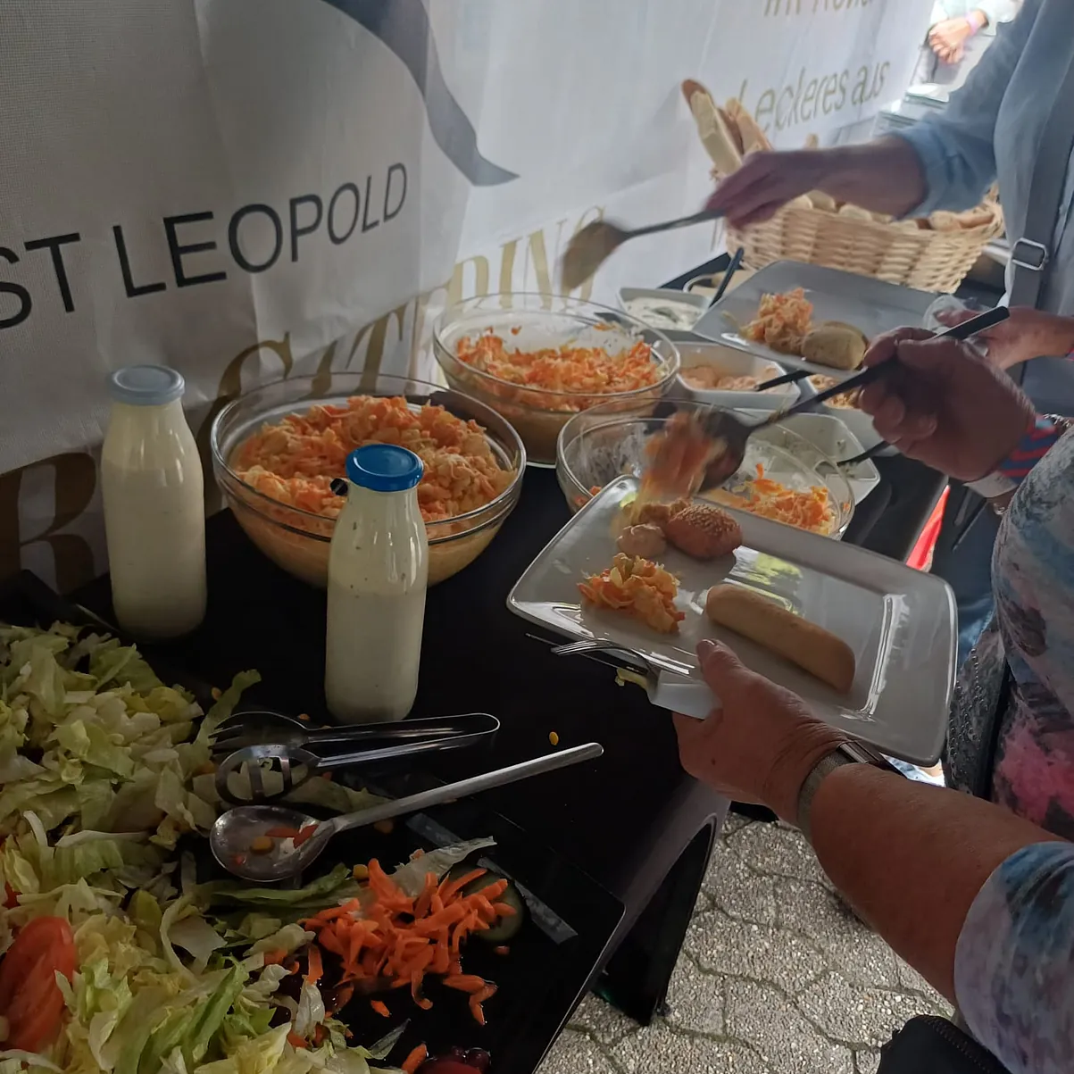 Ein Einblick auf die Salatbar. Man erkennt, das sich Gäste an den Salaten bedienen, wie Krautsalat und gemischten Salat etc. mit Dressings, die man sich selber über den Salat geben kann.